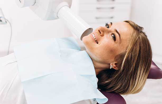 A woman is sitting in a dentist's chair, getting dental x-rays taken and trust in dental xray technology reflected in her smile.